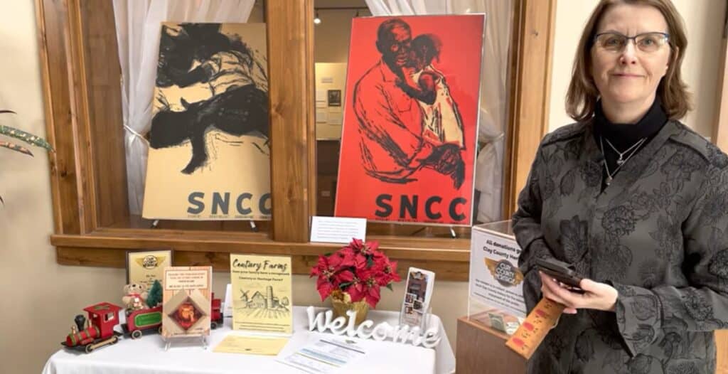 color photo of a woman posing in front of several S-N-C-C posters and a copy of Marion's biography
