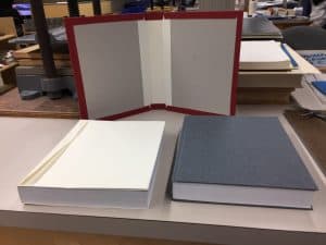 Completed bound book sits to the right of an unbound textblock with an open German lapped casing standing opened behind both objects