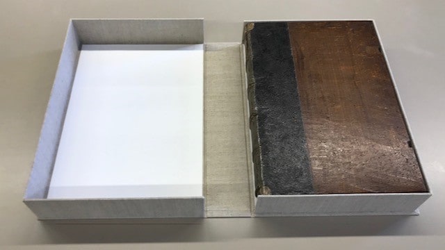 A cloth-covered box lying open to show the rare book housed within.