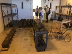 Photo shows rows on cannonballs sitting on the floor and another stack on a cart with HPRH members walking in the background.