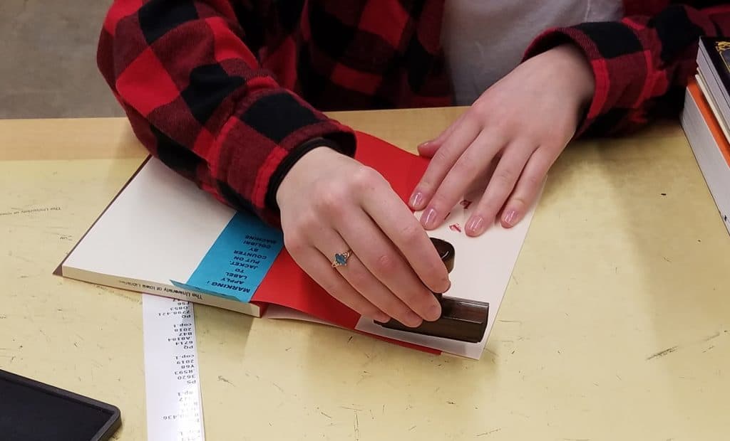 A Library Marking student employee is property stamping the front inside cover of a new book.