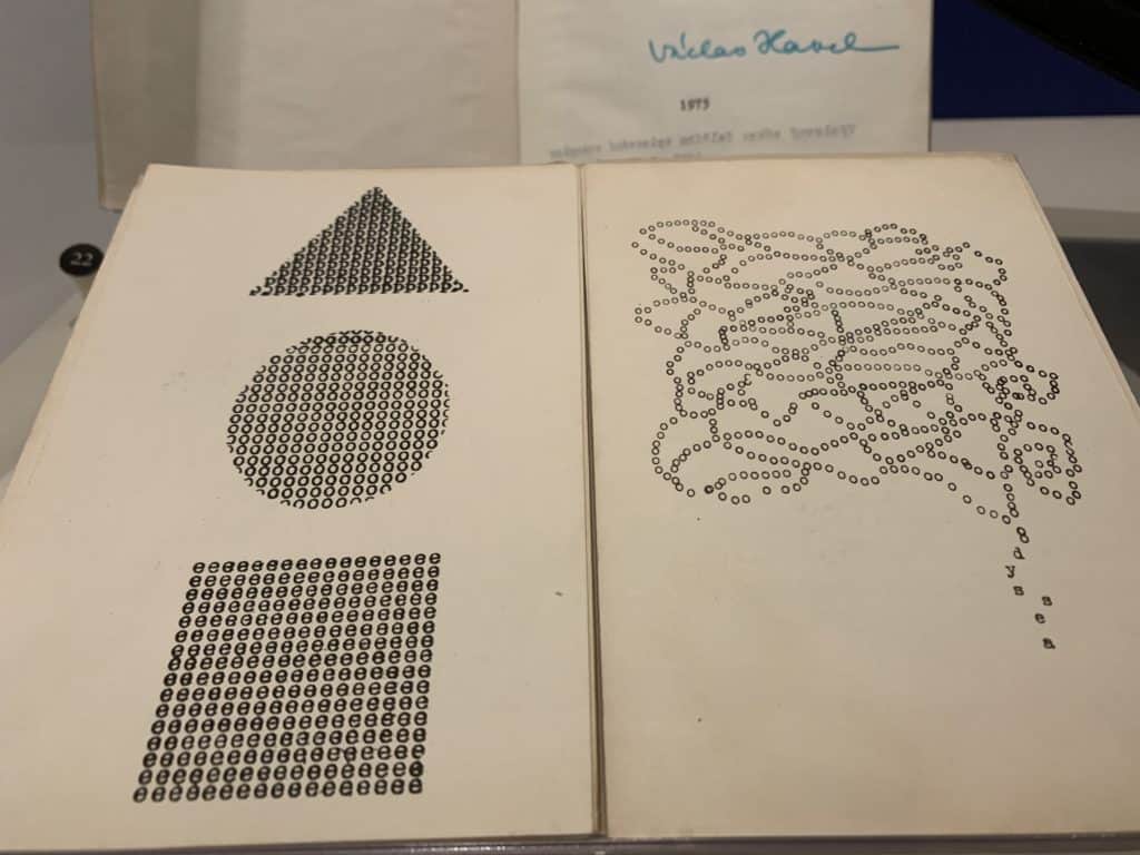 Two books are open in a gallery case. The most prominent features shapes made with typed letters and numbers.