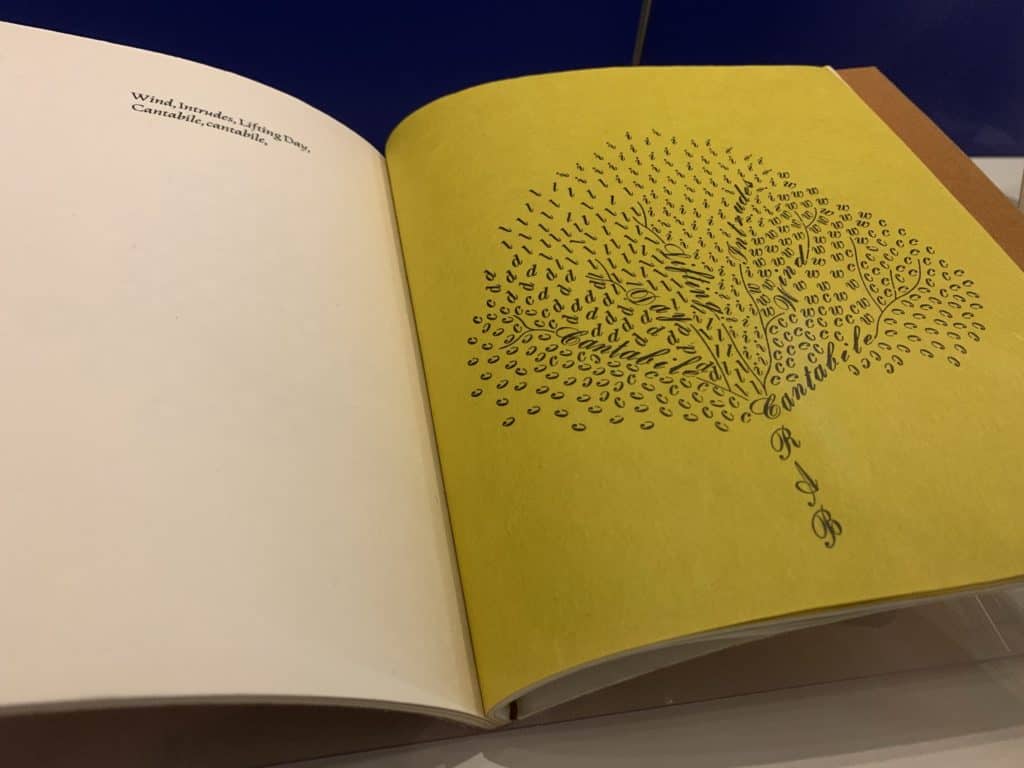 An open book. One page is white and says: Wind, Intrudes, Lifting Day, Cantabile, cantabile. The opposite page is yellow. Those words and a slew of individual letters (C, I, L, R, A, D, W) take the shape of a tree with vibrant branches.