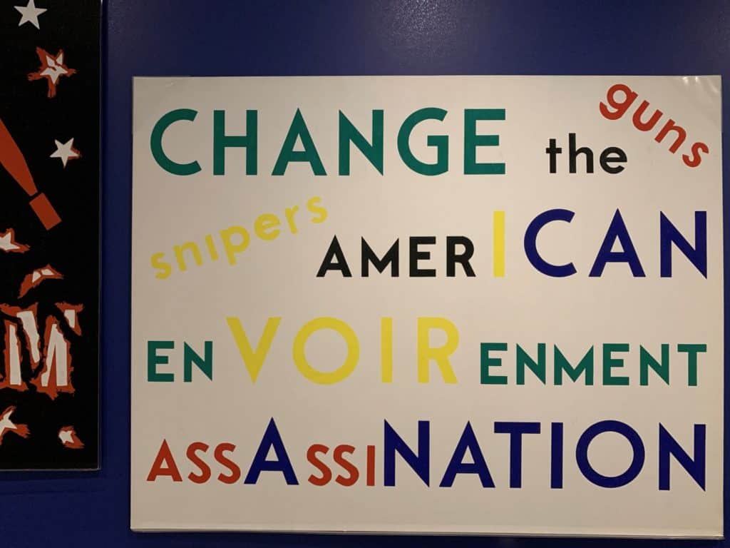 White poster with words in various sizes and primary colors. The words are: Change the American Environment. Guns. Snipers. Assassination.