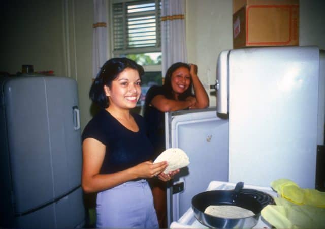 Two women are in the house kitchen. One woman is preparing tortillas.