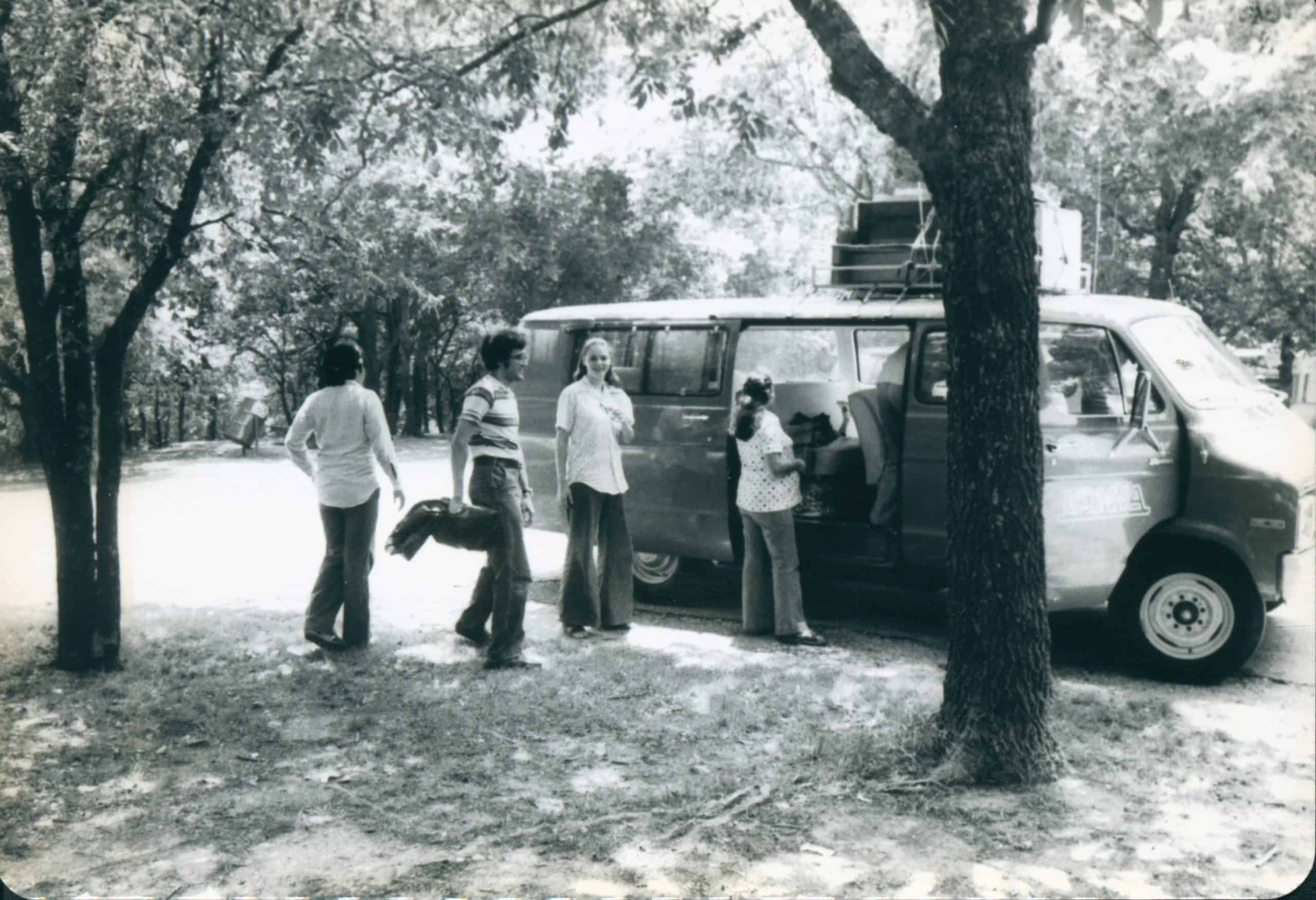 Black and white photo of students standing outside a van on the way to a performance.