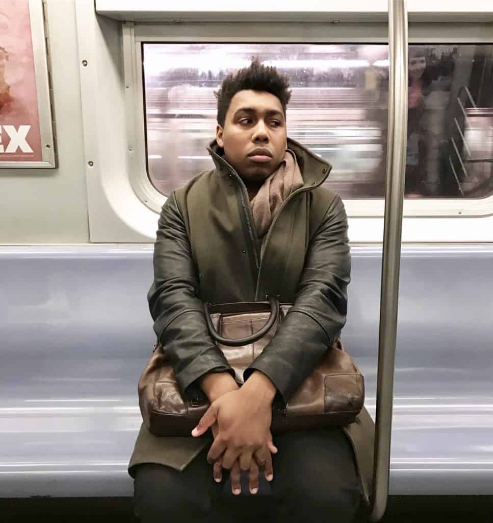 A portrait of Saeed Jones, a Black man who is sitting in a subway car and holding a satchel.