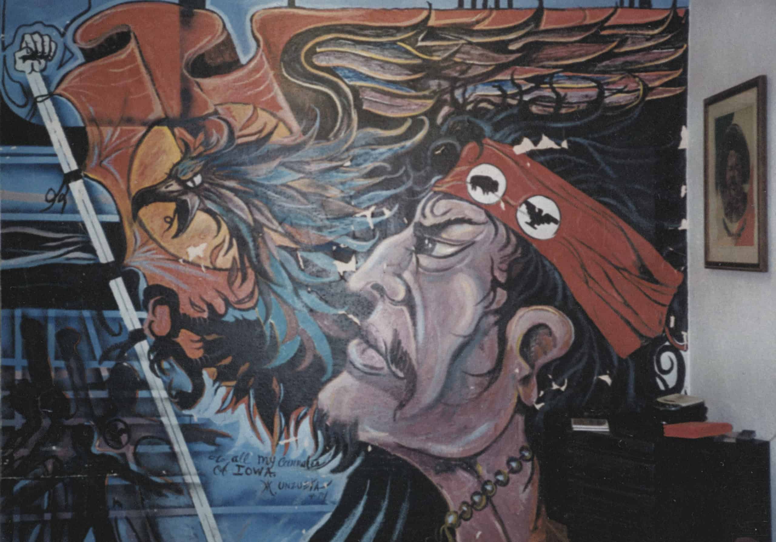 Original mural showing a Latinx man looking forward with determination. A flag and eagle are next to him, and he wears a headband that represents both Latino and Native American causes.