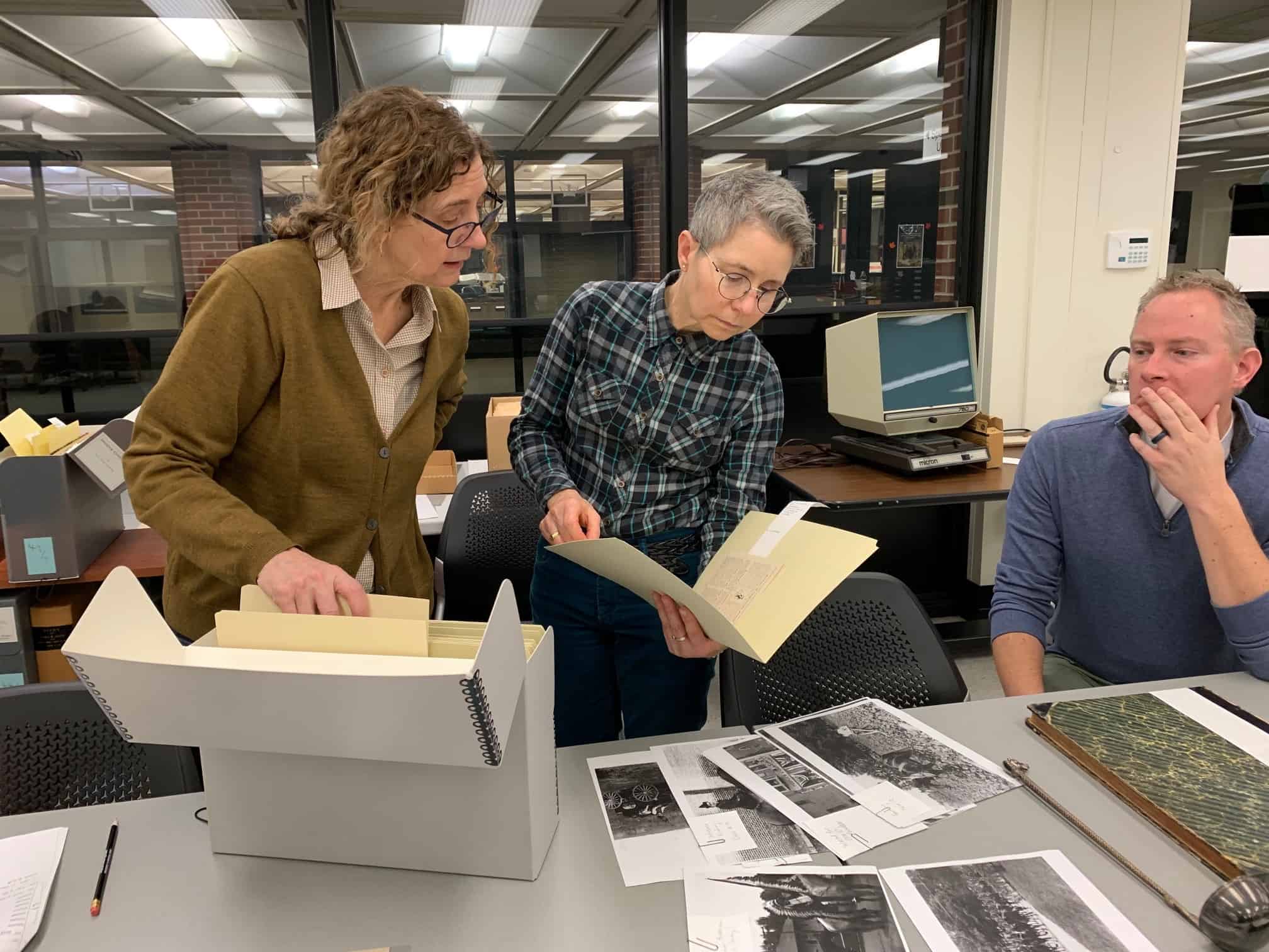 Three people look through archival files as they plan an exhibition for the Main Library Gallery.