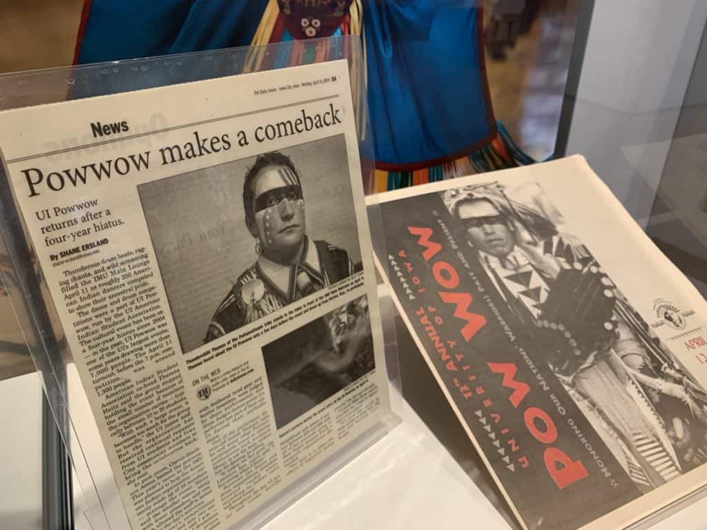 A laminated newspaper article about the University of Iowa Powwow and a printed program from a Powwow are on display together in a case.