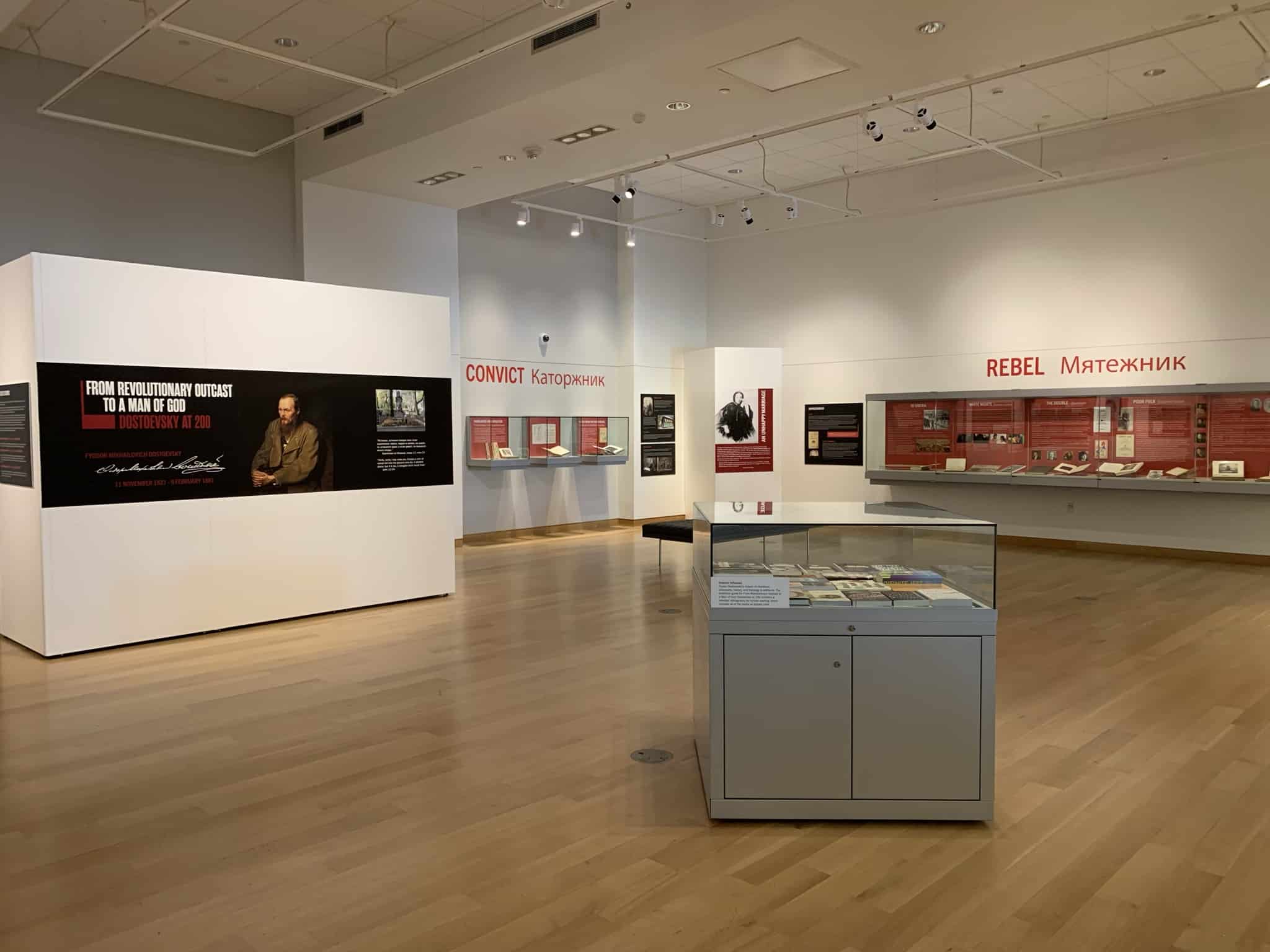 Wide view of the Main Library Gallery featuring a poster with the exhibit title on it. Cases hold books and other objects for display.