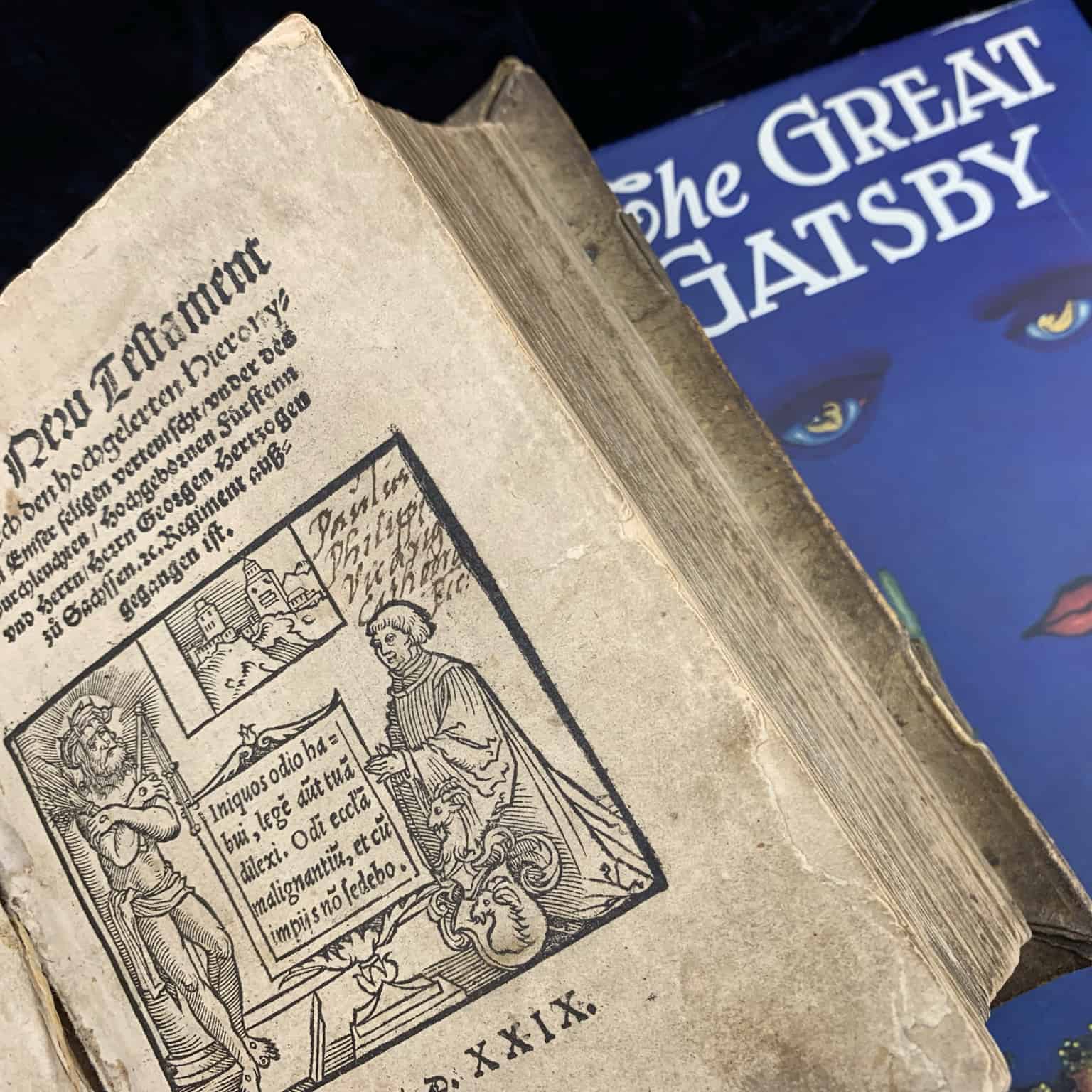 Two books are next to each other. One is a medieval text and another is a copy of The Great Gatsby.