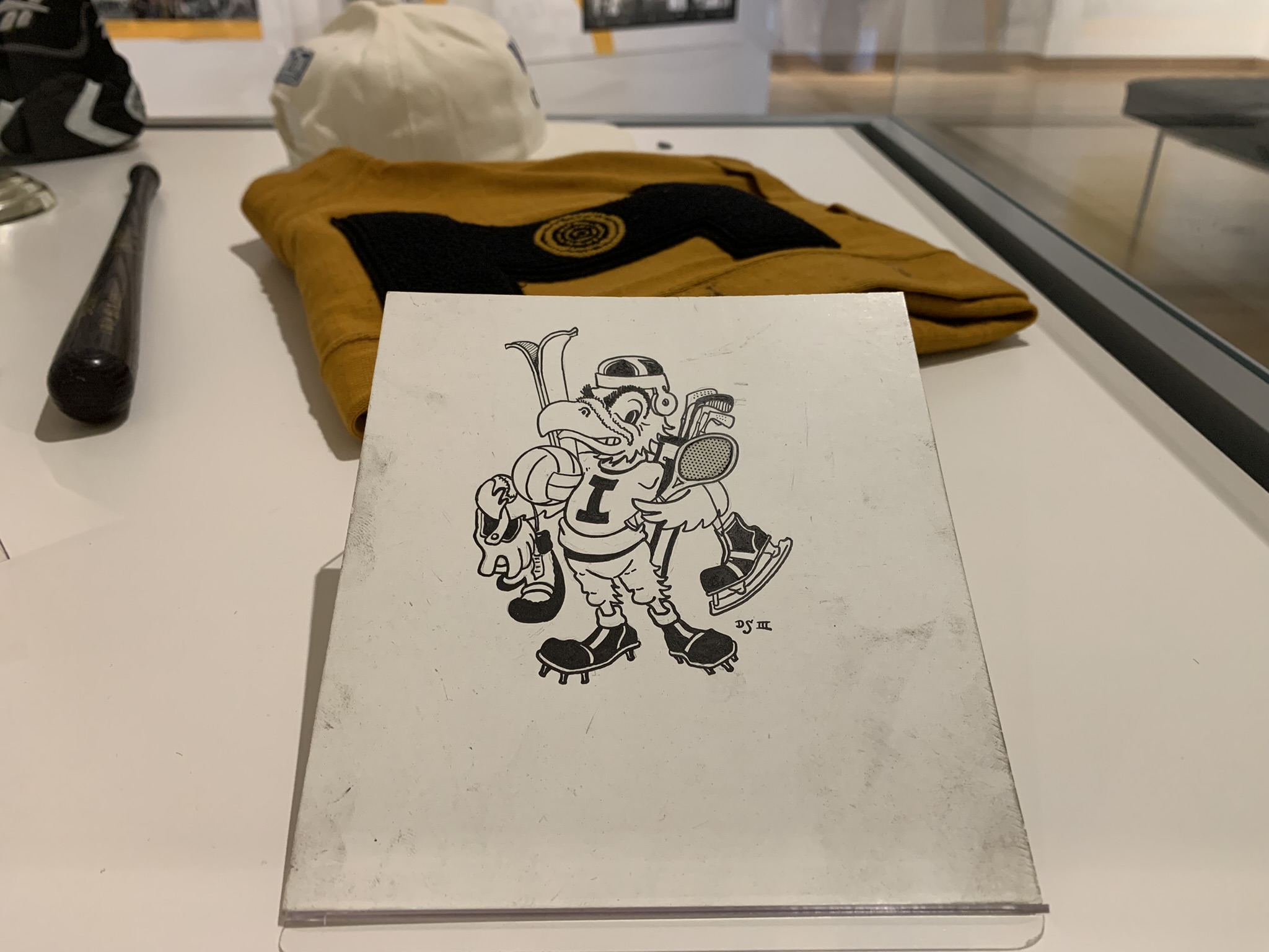 An original black ink drawing of Herky holding various sports equipment. 