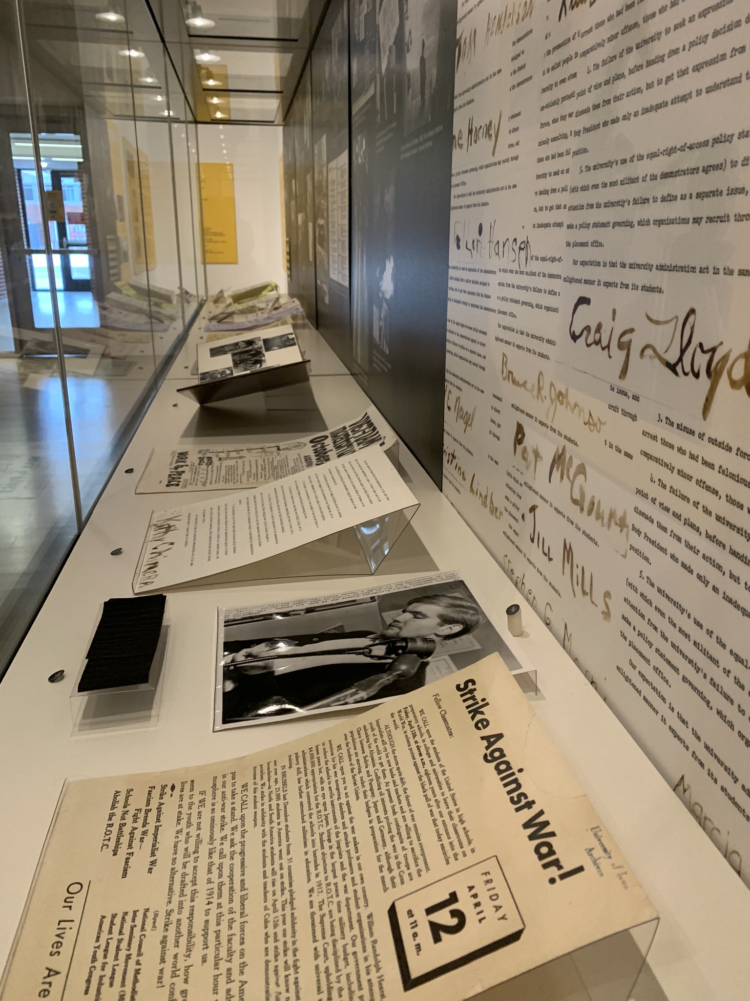 Several flyers protesting various injustices or issues are included in a display case. Most prominently, a black and white photo shows Steve Smith burning his draft card in the 1960s.