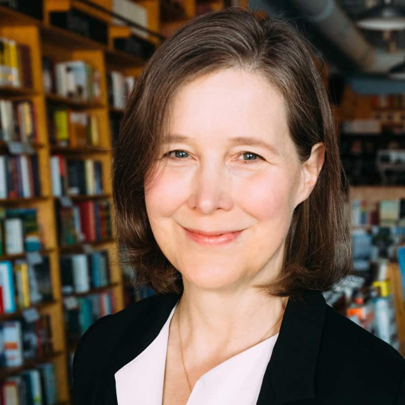 A portrait of author Ann Patchett. She is a white woman with brown hair. Bookshelves are in the background.
