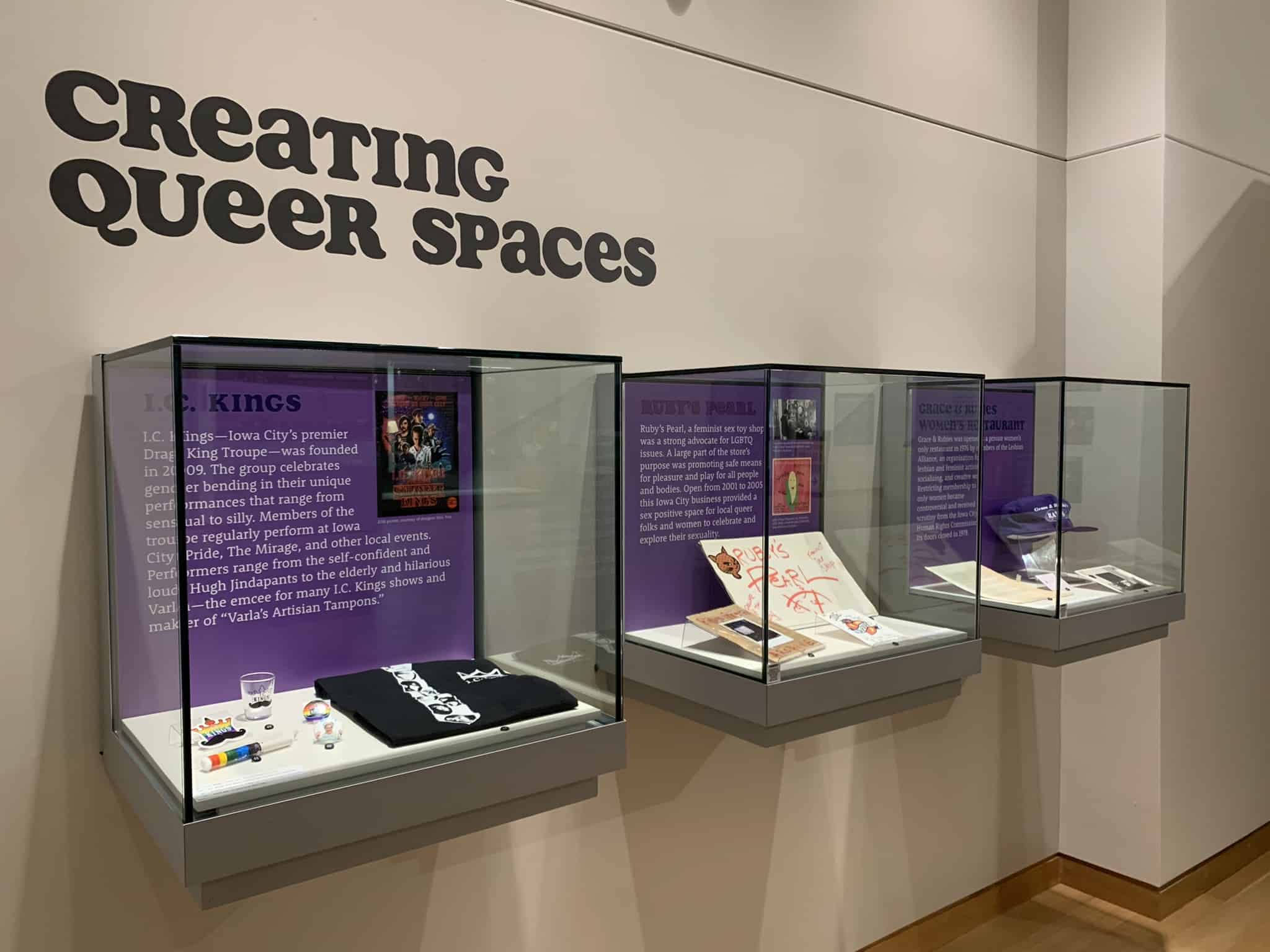 Cases filled with artifacts and walls lined with posters about LGBTQ historical events inside the large Main Library Gallery.