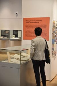 A person stands in front of an exhibit case containing books and ephemera. They are reading an orange text panel.