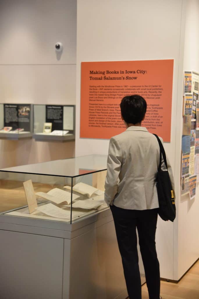 A person stands in front of an exhibit case containing books and ephemera. They are reading an orange text panel.