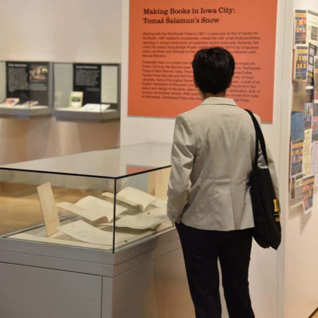 A person stands in front of an exhibit case containing books and ephemera. They are reading an orange text panel.