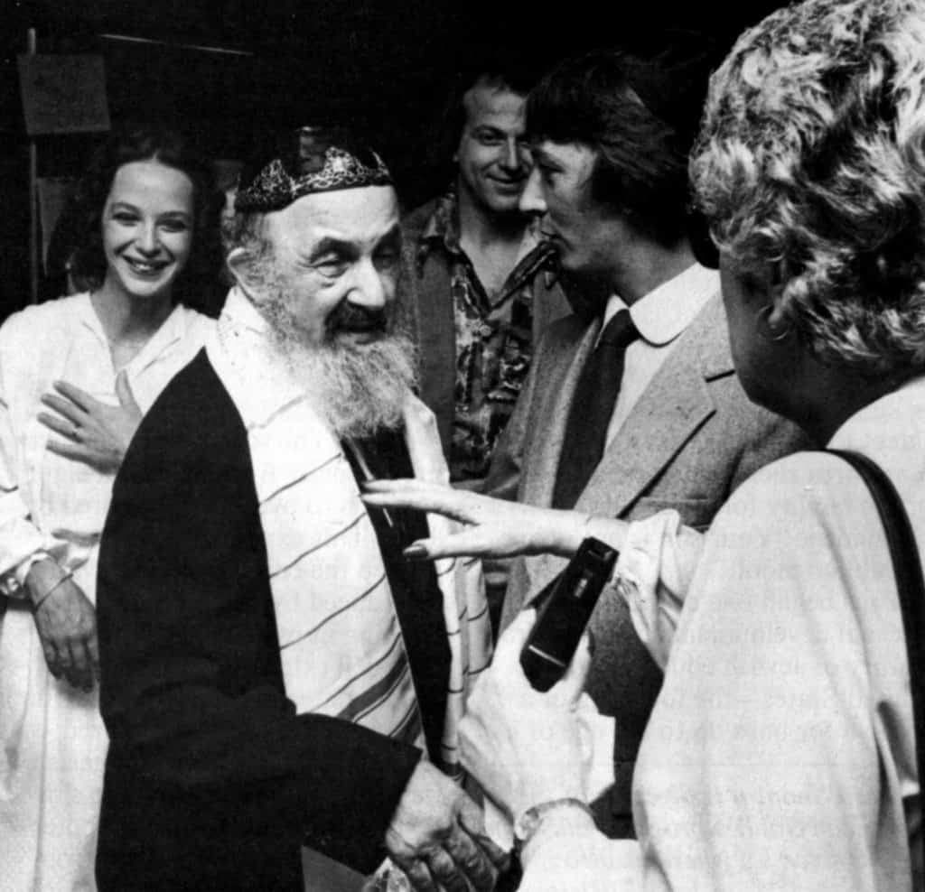 Black and white photo of Bill, an older white man with a gray beard, surrounded by friends. He is wearing a yarmulke and is celebrating his bar mitzvah at age 66.
