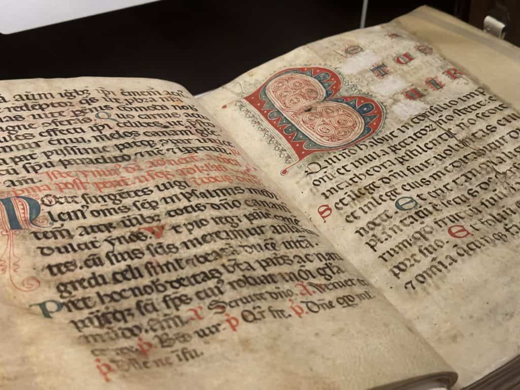 An open book in Latin written in gorgeous medieval calligraphy with a large colorful illumination of the letter B.