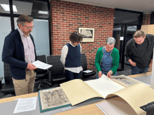 Four people stand in front of a large table. On the table are several large folio books about medical history. The curators are deciding which to include in their exhibit.