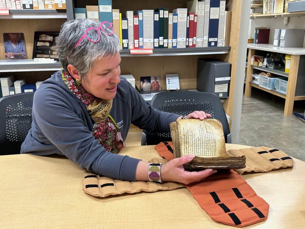Giselle sits at a table and carefully opens a historic psalter book.