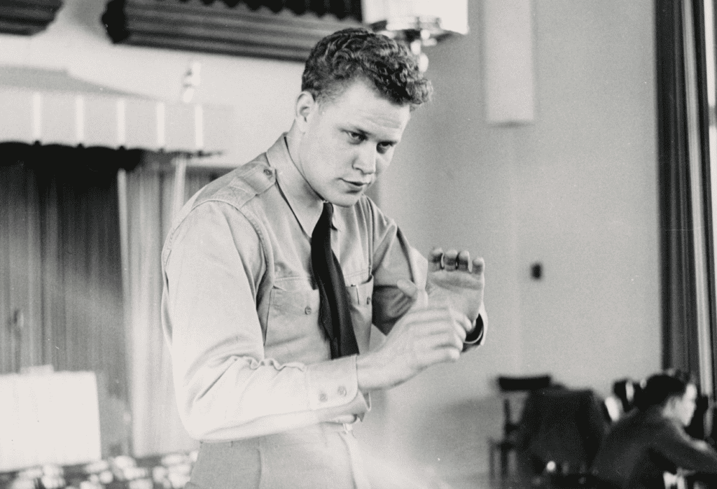 Black and white photo of a young James Dixon in the 1950s. He is wearing his army uniform and conducting an orchestra.