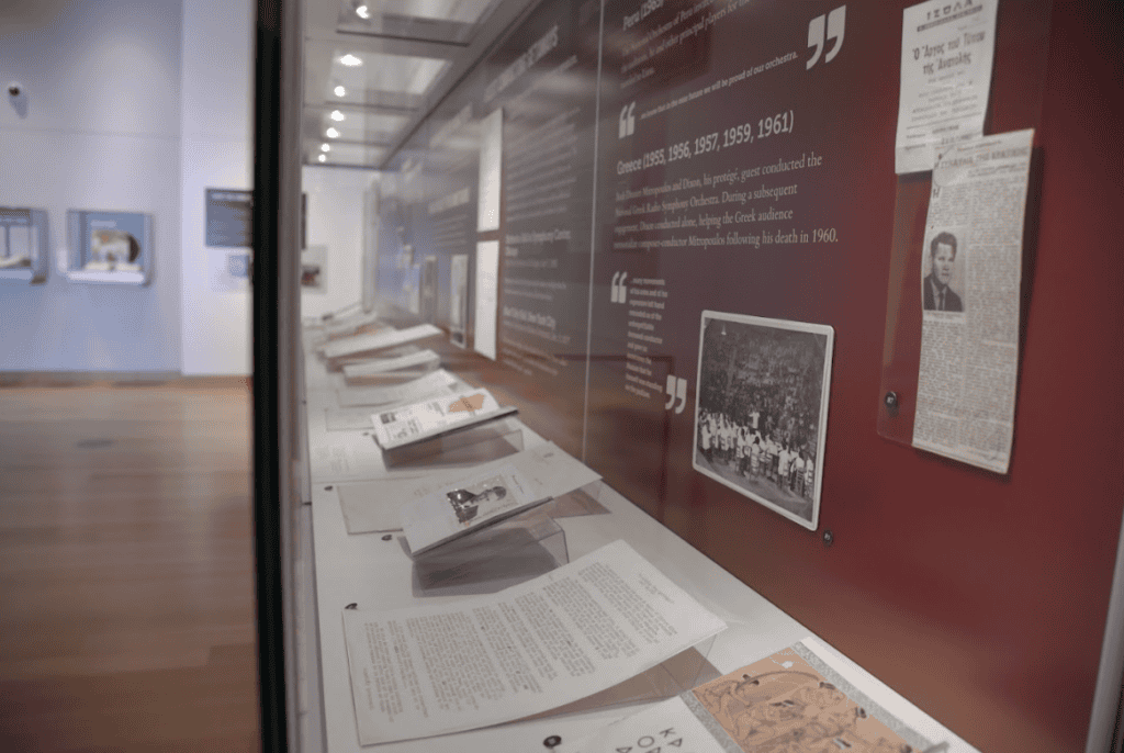 Photo of a long exhibit case filled with paper ephemera like letters, photos, newspaper clippings, and concert programs.