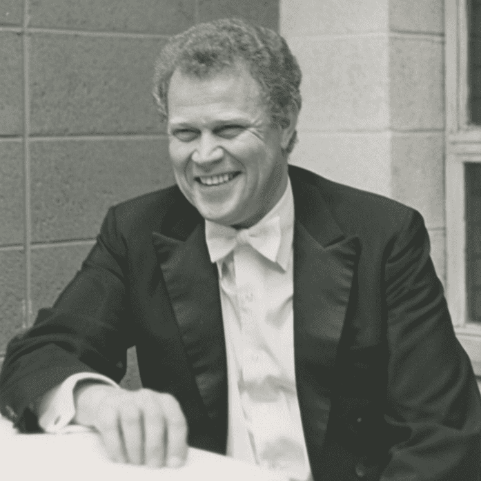 Black and white photo of conductor James Dixon in formal tails. He is smiling and seated.