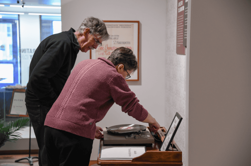 Katie Buehner leans over the record player interactive and shows a visitor how to play the audio.