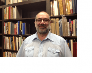 image of white man with glasses standing in front of bookcases