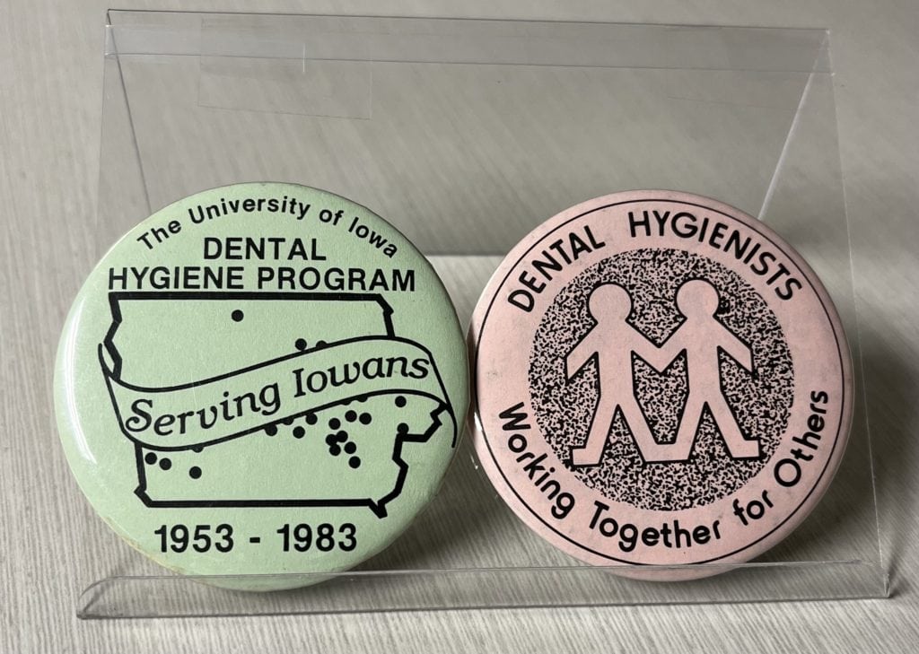 Two pins. On reads "The University of Iowa Dental Hygiene Program Serving Iowans, 1953 to 1983." The other reads "Dental Hygienists: Working Together for Others." 