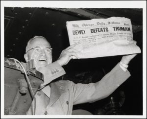 Black and white image of smiling Harry Truman holding a newspaper that says "Dewey Defeats Truman" 