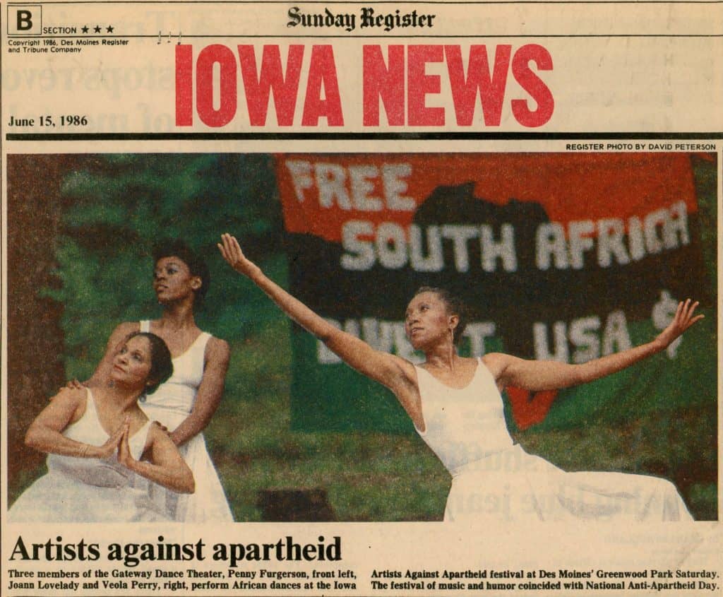 Newspaper showing an image of three dancers in white dresses. A flag behind them says "Free South Africa. Divest USA dollars." 