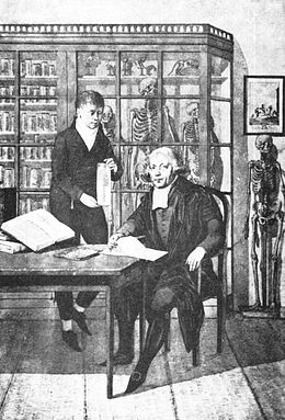 black and white image of Jan Bleuland with another person in room with books and skeletons