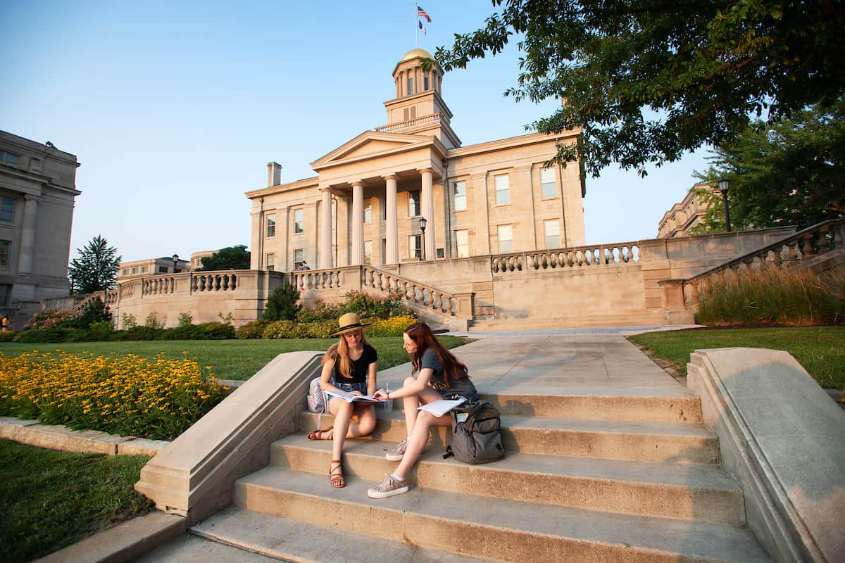 2 women sitting on steps with old capital in background