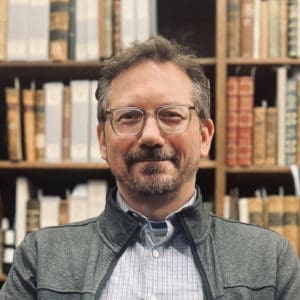 photo of Damien Ihrig, white man, glasses, in front of rare books