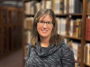 Jennifer Deberg, white woman, glasses, in front of books