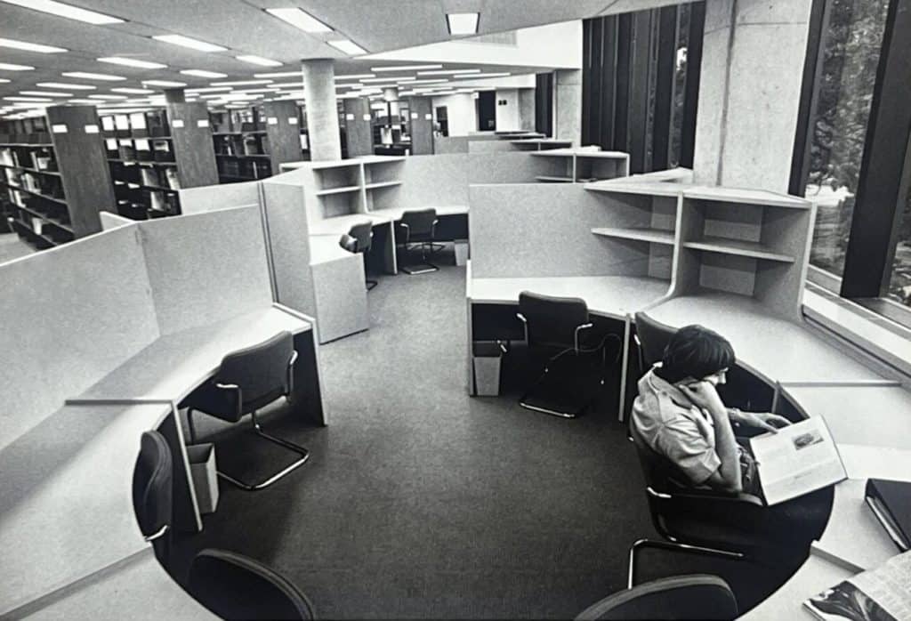 man studying in circular shaped study area, library stacks in background