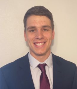 Bryan is in a dark navy suit with a red tie smiling at the camera.