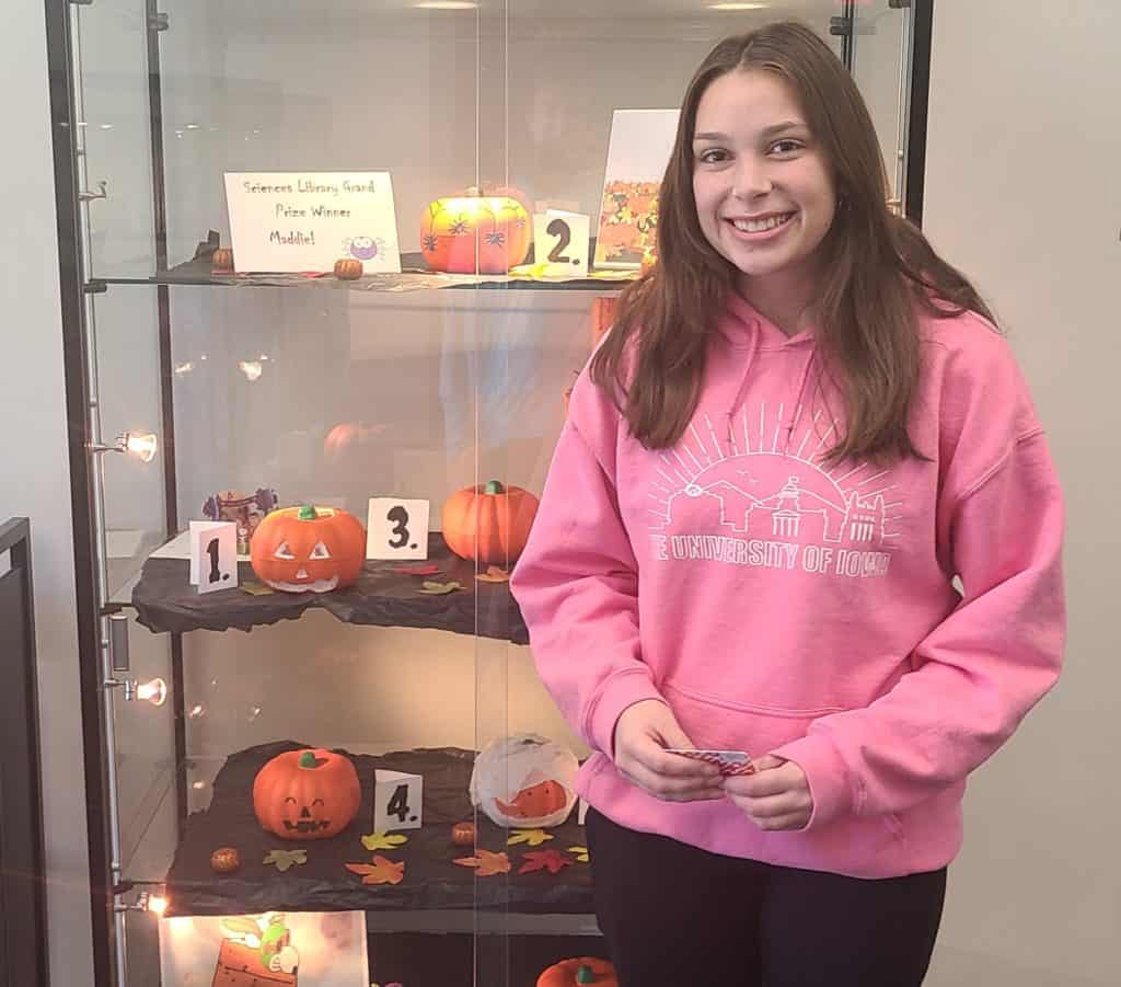a woman holding a giftcard standing in front of a pumpkin display