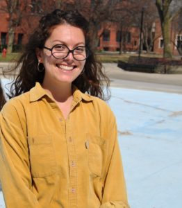 woman in yellow long-sleeved shirt with long dark wavy hair and glasses