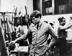 Black and white photo of young man standing at an easel 