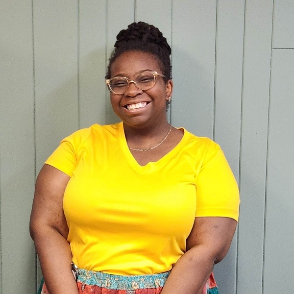 Young Black woman in yellow shirt in front of a grey wall