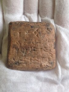 small clay tablet in palm of hand with cuneiform writing on it