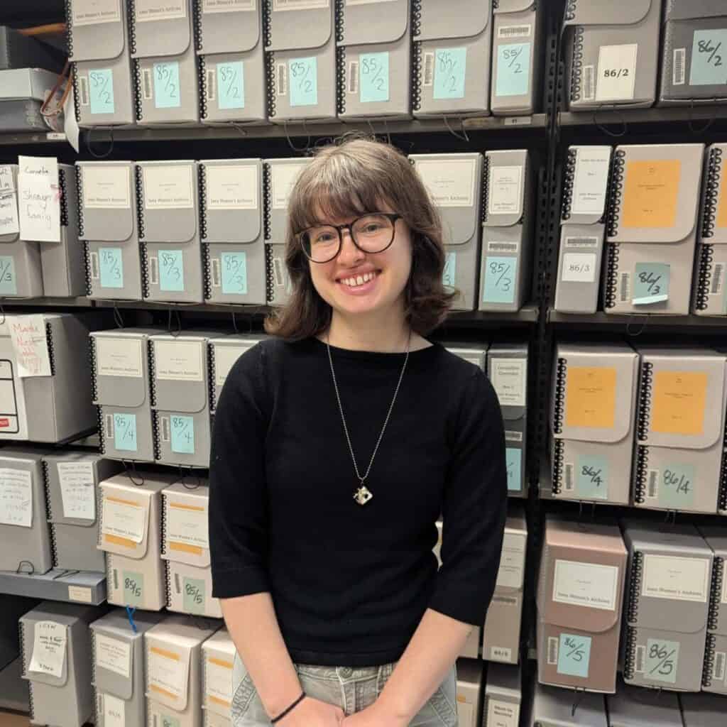 Young woman with glasses and medium brown hair smiles at camera